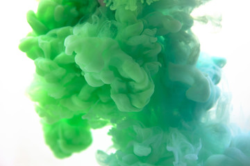 Closeup. Mix of abstract blue and green ink in water on a white background. It looks like smoke or...