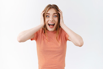 Fototapeta premium Waist-up surprised, amused pretty girl in striped t-shirt, smiling joyfully from amazement, feeling excited hearing awesome news, touch head and stare at unbelievable promo, white background