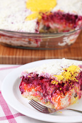 Russian traditional salad named Herring under a fur coat (shuba) on a plate with a fork on a plate
