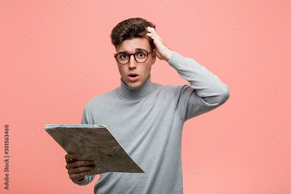 Wall mural Young cool man holding a map cheerful smiles pointing to front.