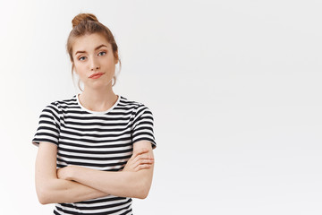 Skeptical sassy young woman in striped t-shirt with messy bun, cross hands chest and smirk, pouting...