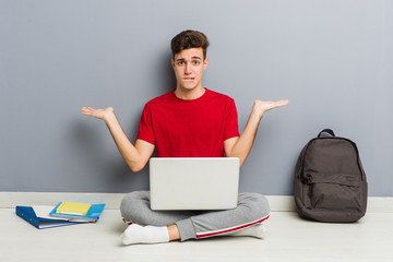 Young student man sitting on his house floor holding a laptop