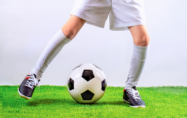Football training for children. Soccer training dribbling. Indoor soccer young player with soccer ball in artificial grass studio. Player in white uniform. Grey background.