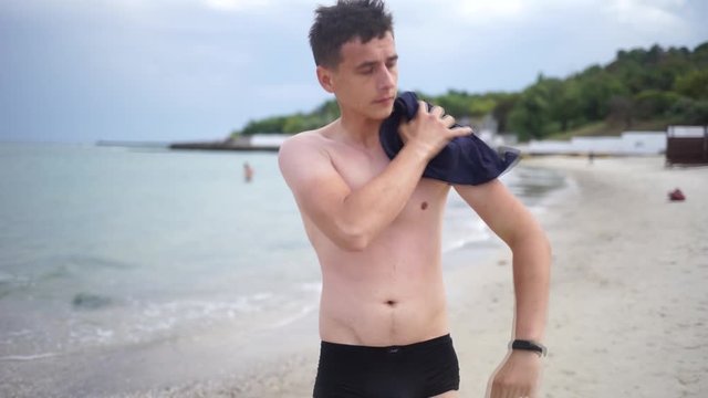A handsome young man wipes the body from the water. A handsome young man on the seashore.Guy with Naked Torso Wiping His body.