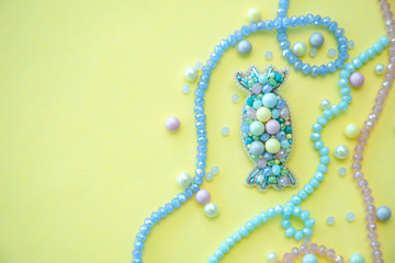 Handmade candy brooch in pastel colors, fashion jewelry, girl and women accessory on yellow background with copy space, flat lay with beads, pearls and crystals
