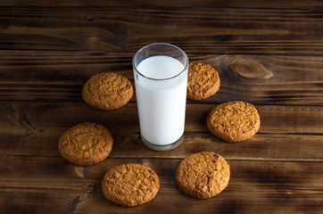 Stack of oatmill cookies and milk glass on wooden surface