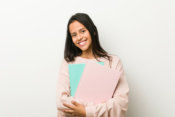 Naklejka premium Young hispanic woman holding some notebooks happy, smiling and cheerful.