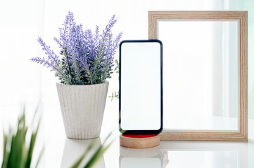 Mockup smartphone with blank screen, wooden frame and houseplant on white top table.