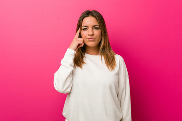 Fototapeta premium Young authentic charismatic real people woman against a wall pointing temple with finger, thinking, focused on a task.