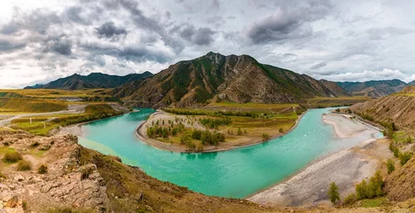 Foto op Canvas Panorama of mountain river on background of beautiful mountains in cloudy weather. View of turquoise river in the mountains on the background gloomy sky © timofeev
