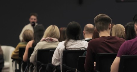 Blur background of educational business training. Student science conference at university campus, man speaker talking microphone for audience, view from auditorium sitting back to camera.