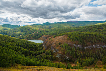 Panorama of mountain lake on background of beautiful snowy mountain peaks in cloudy weather. Mountain lake in the forest. View of lake on the background of blue sky