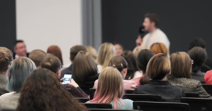 Business training for startup company from entrepreneur, view from audience. Man speaker talking about successful marketing and management for people startuppers in large crowded auditorium.