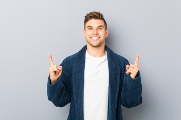 Young caucasian man wearing pajama indicates with both fore fingers up showing a blank space.