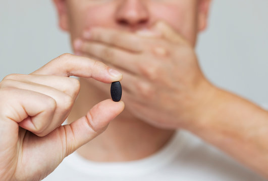 man holds a black pill, closes his mouth with his hand, refusing medicine, protest,