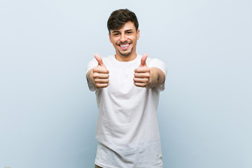 Young caucasian man wearing a white tshirt with thumbs ups, cheers about something, support and...