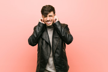 Fototapeta premium Young hispanic man wearing a leather jacket covering ears with hands.