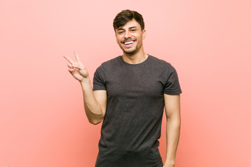 Young hispanic casual man joyful and carefree showing a peace symbol with fingers.
