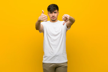 Young hispanic casual man showing thumbs up and thumbs down, difficult choose concept