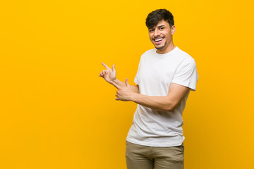 Young hispanic casual man pointing with forefingers to a copy space, expressing excitement and...