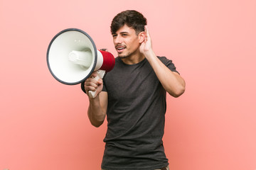 Young hispanic man holding a megaphone trying to listening a gossip.
