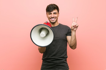 Young hispanic man holding a megaphone showing number two with fingers.