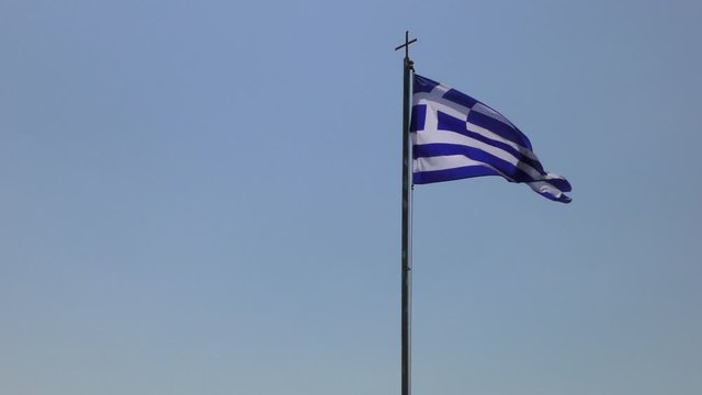Monasteries in Meteora, Greece. Orthodox cross on the flagpole and flag of Greece on a background of a bright blue sky.