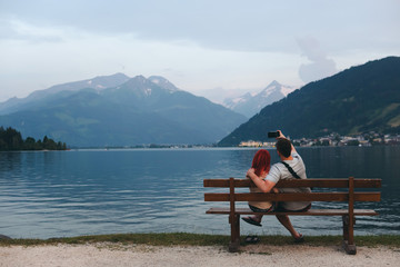 A young couple on the lake take pictures, take selfies, enjoy the views, vacation, relax. couple in love Zell am see in Austria, copy space, selective focus, summer day