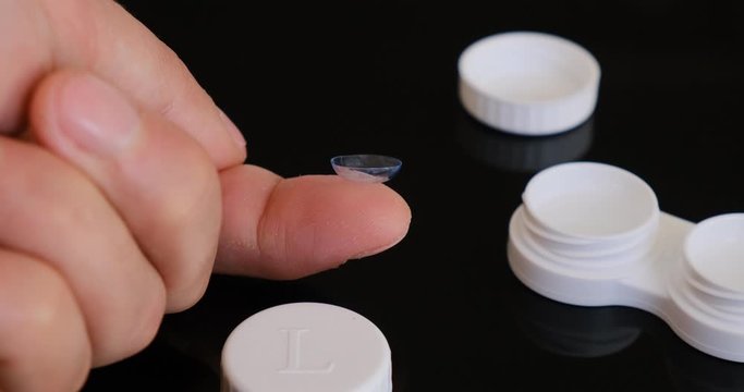 Transparent toric contact lens on a fingertip - closeup details.