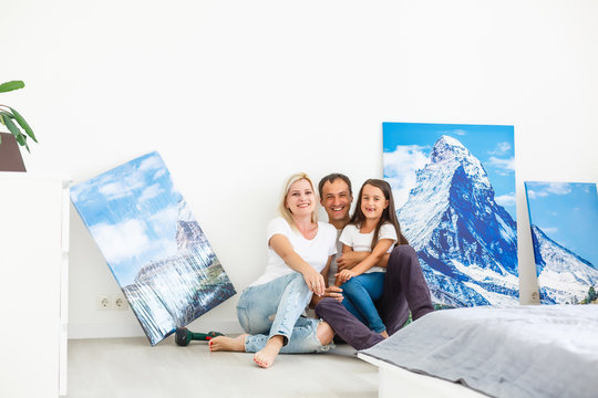 In new flat family hangs a large photo canvas on empty white wall at home