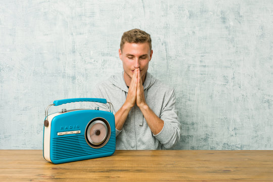 Young caucasian man listening to the radio holding hands in pray near mouth, feels confident.
