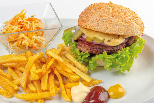 fast food menu. hamburger, french fries and salad. burger with beef stake, cheese onion and pickle. mayonnaise ketchup mustard on the white plate. healthy variation of junk food. close up view