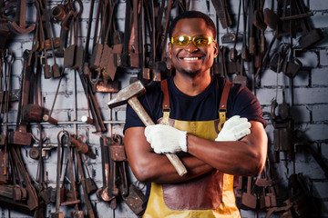 hammer industry small business concept.african american man dressed in historical clothing is hammering on the anvil. A blacksmith forges a metal product
