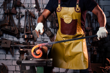 hammer industry small business concept.african american man dressed in historical clothing is hammering on the anvil. A blacksmith forges a metal product