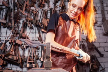 redhaired ginger young european feminist woman wearing leather apron working blacksmith...