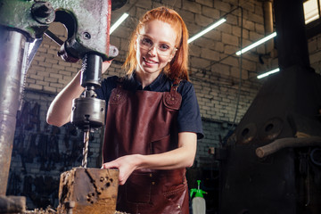 redhaired ginger young european feminist woman wearing leather apron working blacksmith workshop.small business strong and independent concept