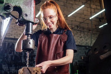 redhead ginger woman working smithytools in dark workplace forging hammering malleation details. small business concept