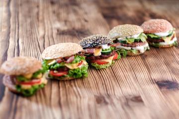 5 handmade burgers with beef, salad, cheese tomatoes, sesame seeds, bacon on brown wooden table