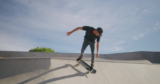 Skateboarder jumping over a concrete hip feature in a skatepark on a sunny day, slow motion skateboarding moves