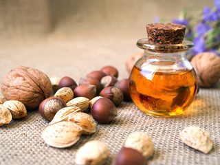 A bottle of aroma oil, almonds, walnuts, hazelnuts and blue flowers on jute background. Set of organic cosmetic products, selective focus