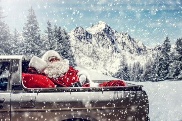 Bearded in red clothes sits on the back of a white truck.Santa distributes gifts for children.Landscape of mountains and winter forest covered with snow and frost.Christmas time.Copy space.Snowflakes 