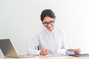 Smiling caucasian businesswoman working on laptop and taking notes in modern office. Smart businesswomen happy smiling on her work.