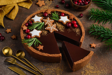 Gingerbread chocolate tart decorated with rosemary, cranberries and gingerbread stars. Christmas dessert. Slice of tarte