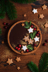 Chocolate tart with a gingerbread cookie base, decorated  with gingerbread, cranberries and rosemary on a wooden background. Christmas concept