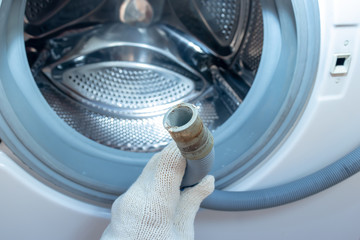 Hand of a plumber holding a broken flexible drain hose of washing machine, clogged and covered with...