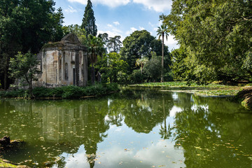 Fototapeta na wymiar The pond at the English Garden of Caserta Royal Palace. In the middle, there is a small island with fake ruins of a temple