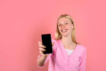 Fototapeta premium Happy girl holds smartphone with empty screen. Communication and technology concept. Smile girl with mobile phone. Black Friday, cyber Monday. Advertising new model. Beautiful woman shows smart phone.