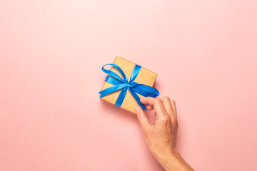 Female hand holds a gift on a pink background. Gift concept for a loved one, holiday, christmas. Flat lay, top view