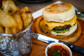 Tasty grilled home made beef burger with lettuce and cheese on a rustic wooden table of counter
