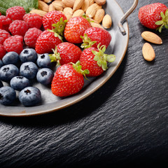 Tray with ripe organic bilberry raspberry strawberry and almonds set on slate closeup